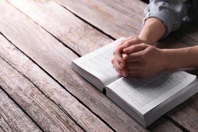 Photo of Religion. Christian woman praying over Bible at wooden table, closeup. Space for text