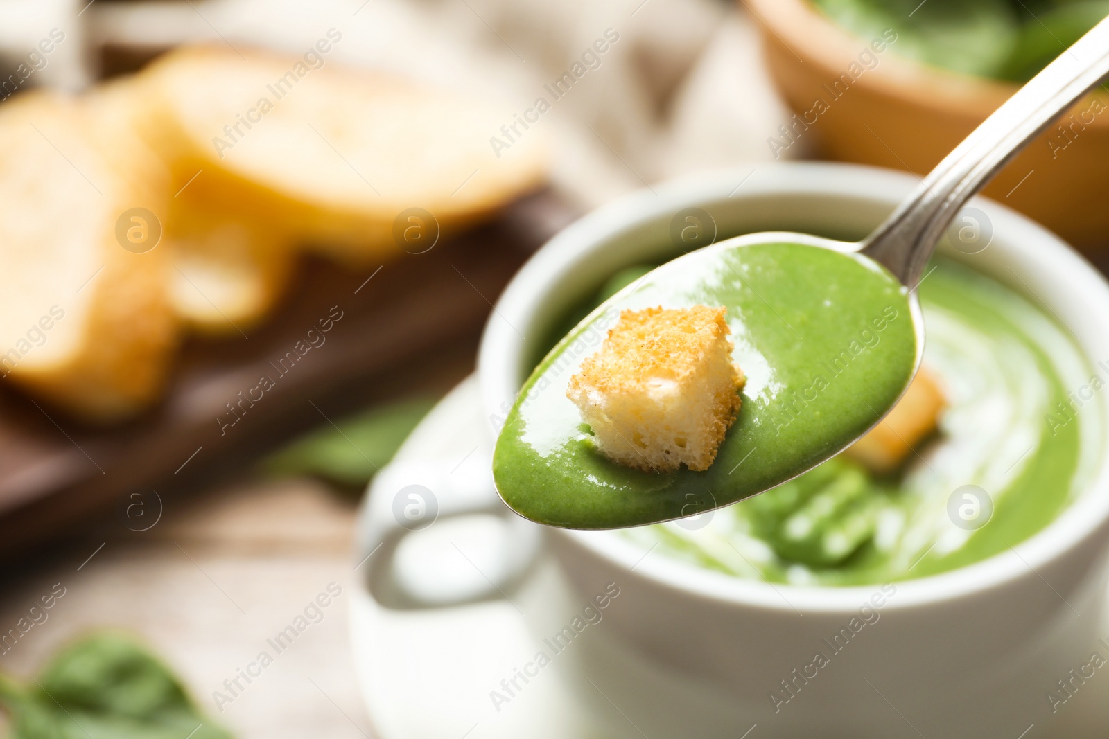 Photo of Spoon with fresh vegetable detox soup and crouton on blurred background, closeup