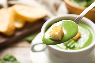 Photo of Spoon with fresh vegetable detox soup and crouton on blurred background, closeup