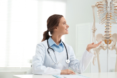 Female orthopedist at table near human skeleton model in office