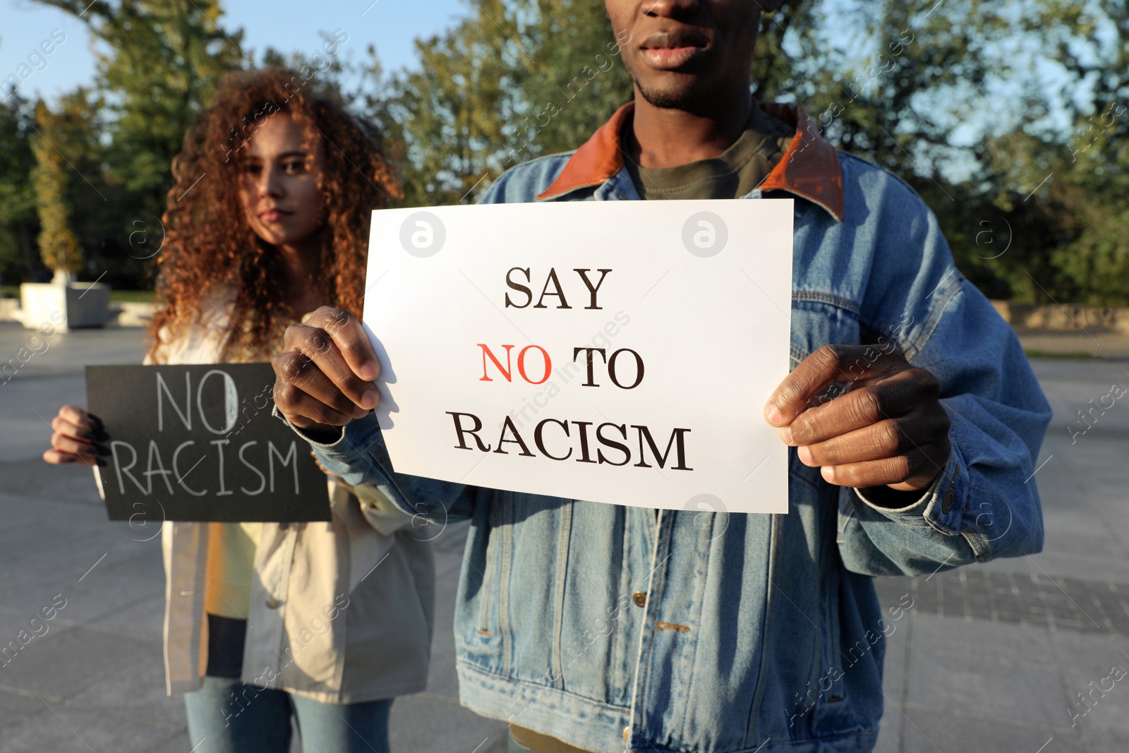 Photo of African American woman and man holding signs with phrase Say No To Racism outdoors, closeup