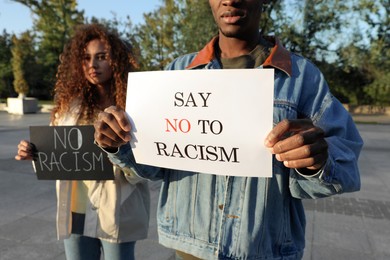 Photo of African American woman and man holding signs with phrase Say No To Racism outdoors, closeup