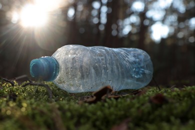 Photo of Used plastic bottle on grass in forest, closeup. Recycling problem
