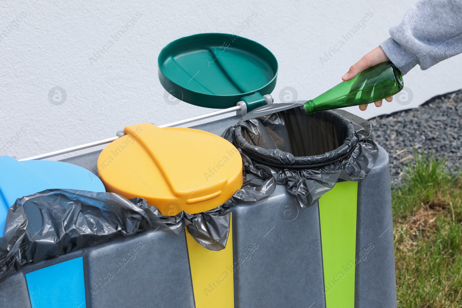 Photo of Woman throwing glass bottle in bin outdoors, closeup. Recycling concept