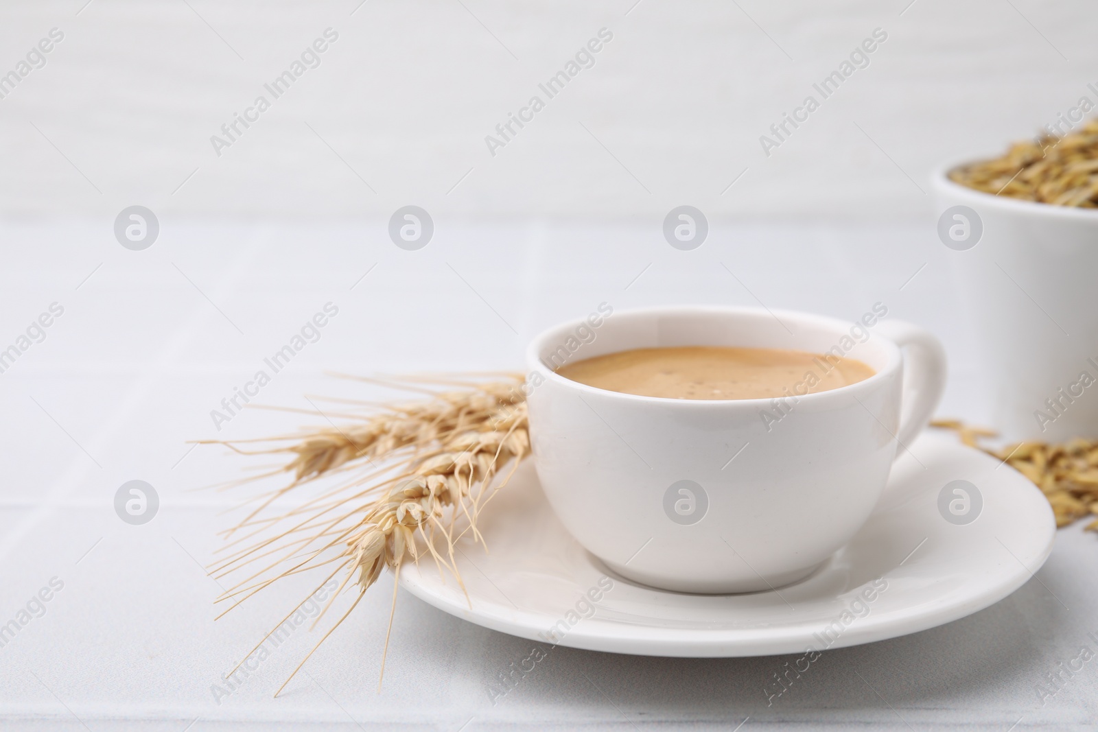 Photo of Cup of barley coffee, spikes and grains on white table, closeup. Space for text