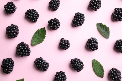 Tasty ripe blackberries and leaves on light pink background, flat lay