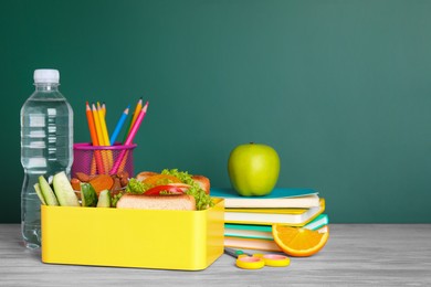 Photo of Lunch box with healthy food and different stationery on wooden table near green chalkboard, space for text