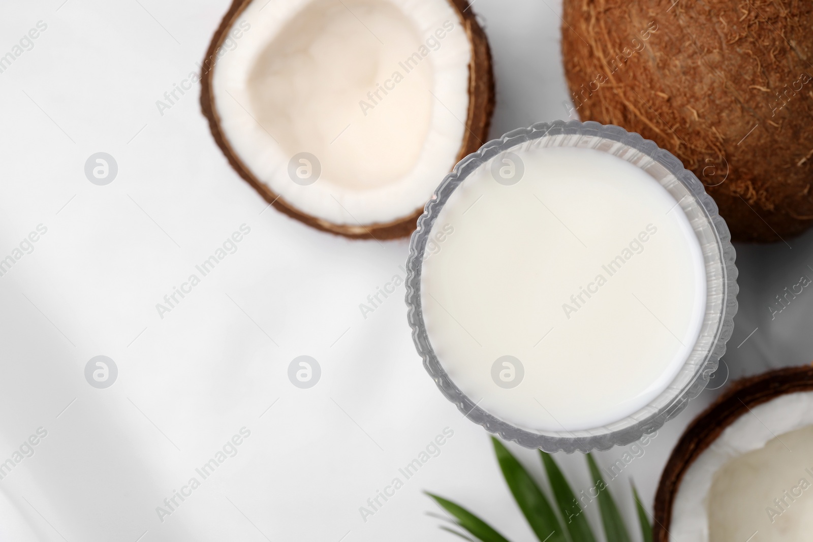 Photo of Glass of delicious coconut milk, palm leaf and coconuts on white table, flat lay. Space for text