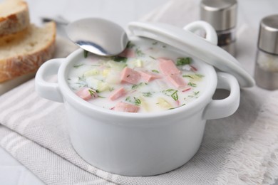 Photo of Delicious cold summer soup (okroshka) with boiled sausage in pot and spoon on white table