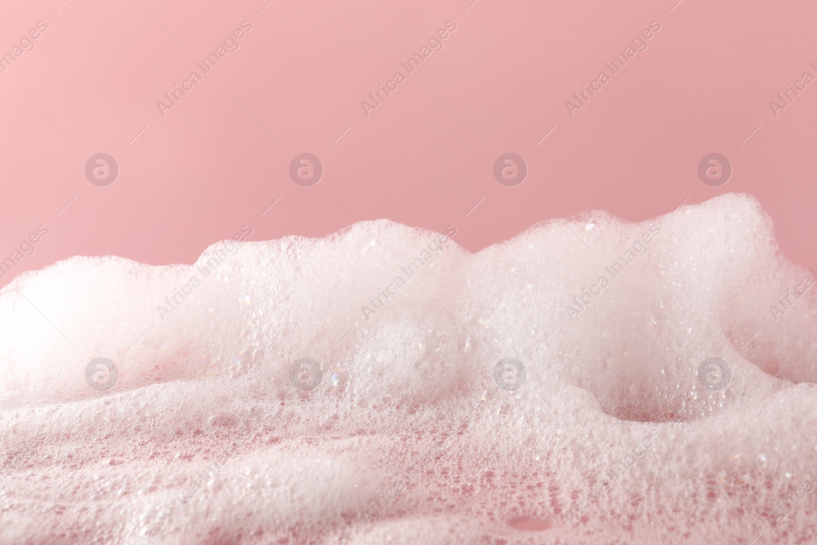 Photo of Fluffy bath foam on pink background, closeup. Care product