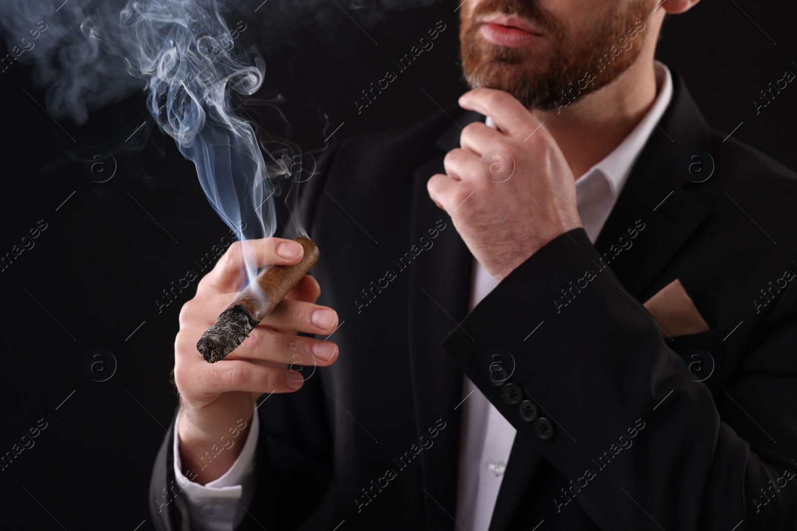 Photo of Man in elegant suit smoking cigar on black background, closeup