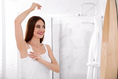 Photo of Beautiful young woman applying deodorant in bathroom. Space for text