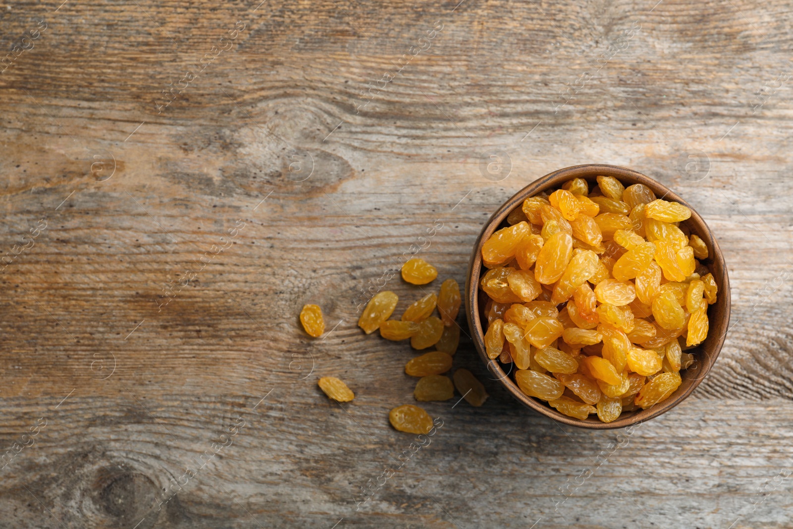 Photo of Bowl with raisins and space for text on wooden background, top view. Dried fruit as healthy snack