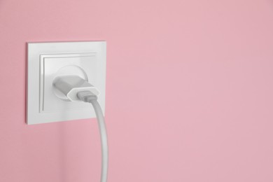 Charger adapter plugged into power socket on pink wall, space for text. Electrical supply