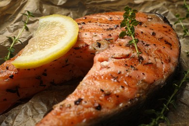 Tasty grilled salmon steak, lemon slices and thyme on parchment paper, closeup