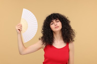 Woman with hand fan suffering from heat on beige background