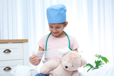 Photo of Cute child playing doctor with stuffed toy in hospital ward