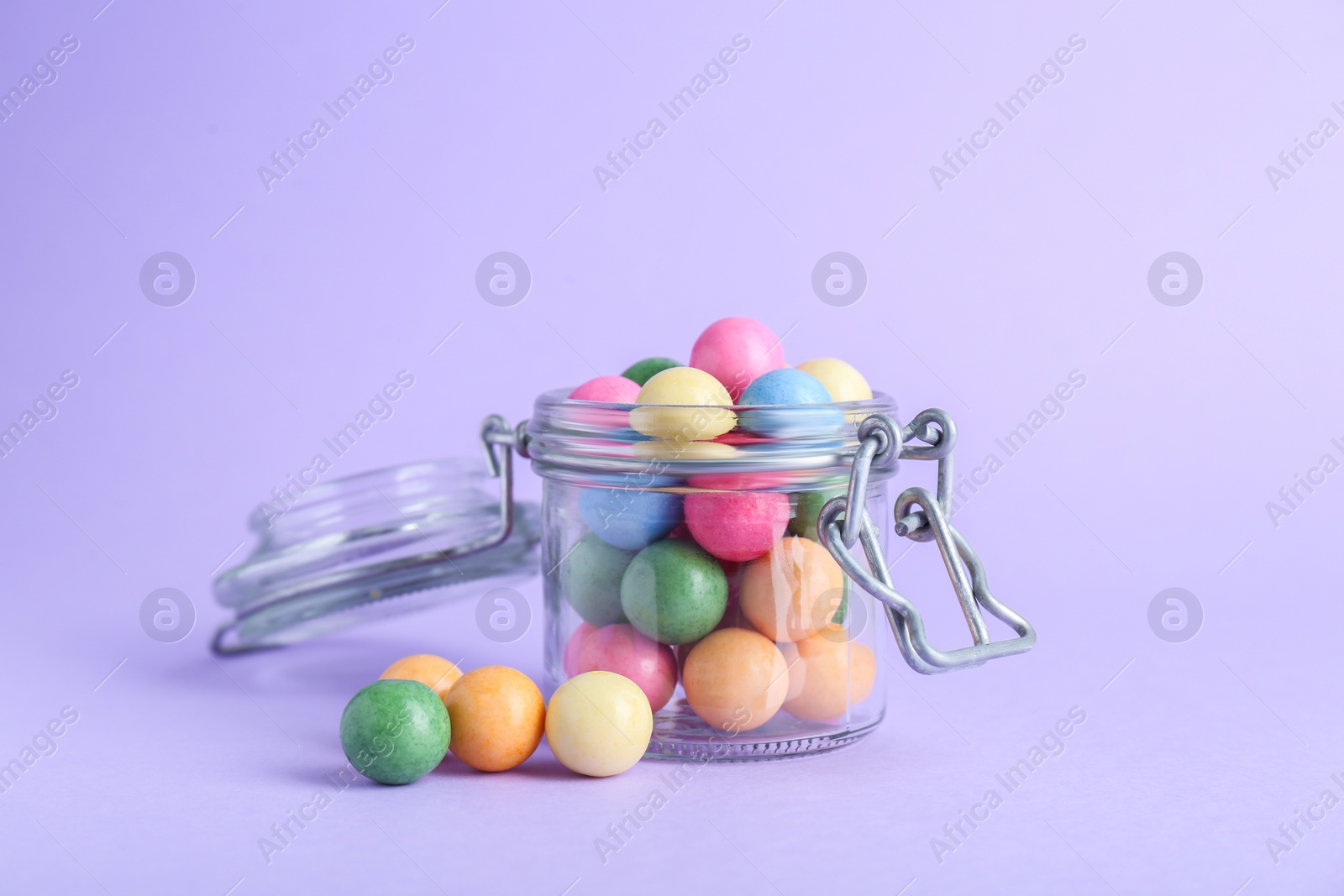 Photo of Jar with many bright gumballs on lilac background