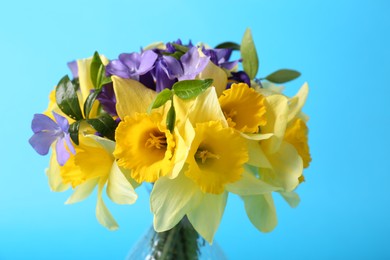 Photo of Bouquet of beautiful yellow daffodils, iris and periwinkle flowers in vase on light blue background, closeup
