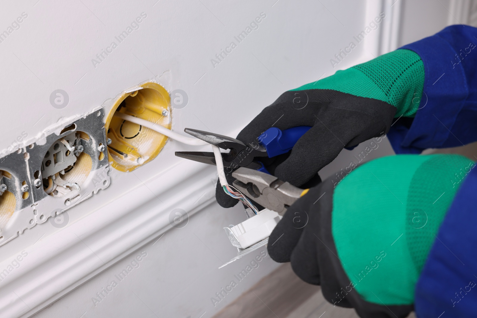 Photo of Professional repairman fixing power sockets with pliers indoors, closeup