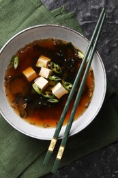 Photo of Bowl of delicious miso soup with tofu and chopsticks on black textured table, top view