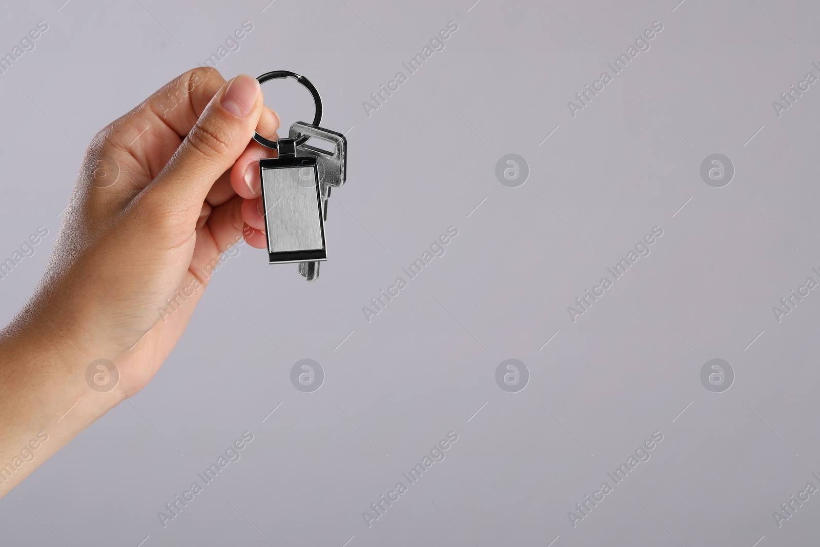 Photo of Woman holding key with metallic keychain on grey background, closeup. Space for text