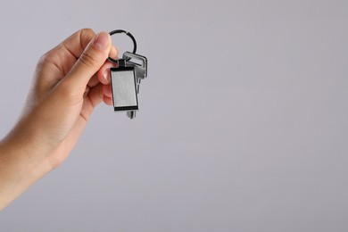 Photo of Woman holding key with metallic keychain on grey background, closeup. Space for text