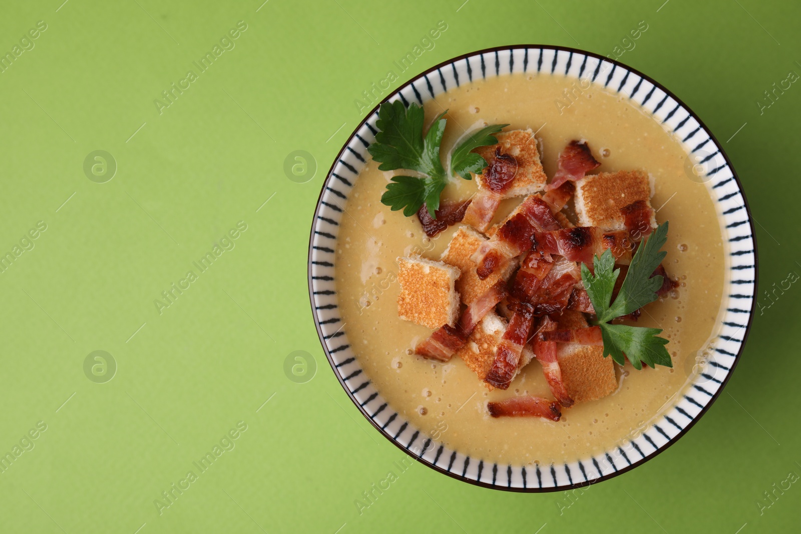 Photo of Delicious lentil soup with bacon and parsley in bowl on green table, top view. Space for text