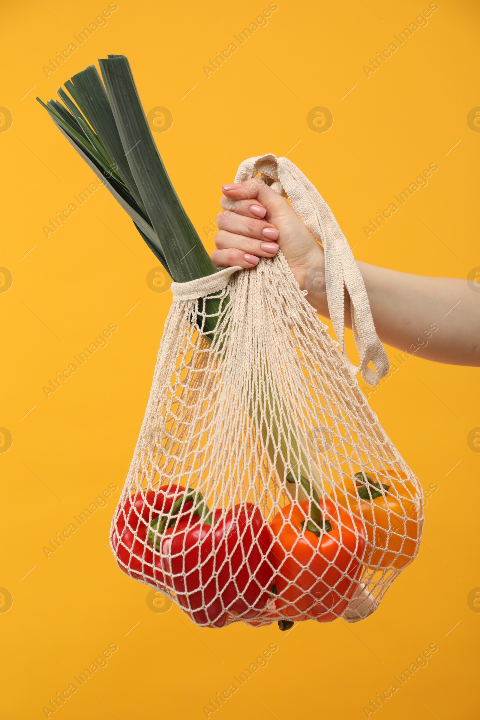 Photo of Woman with string bag of fresh vegetables on orange background, closeup