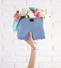 Photo of Woman holding elegant handbag with spring flowers against white brick wall, closeup