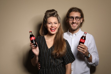 Photo of MYKOLAIV, UKRAINE - NOVEMBER 28, 2018: Young couple with bottles of Coca-Cola on color background