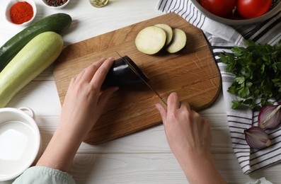 Photo of Cooking delicious ratatouille. Woman cutting fresh eggplant at white wooden table, top view