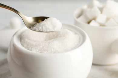 Photo of Taking spoon of white sugar from ceramic bowl on table, closeup