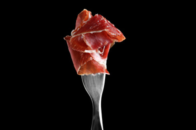 Tasty prosciutto on fork against black background