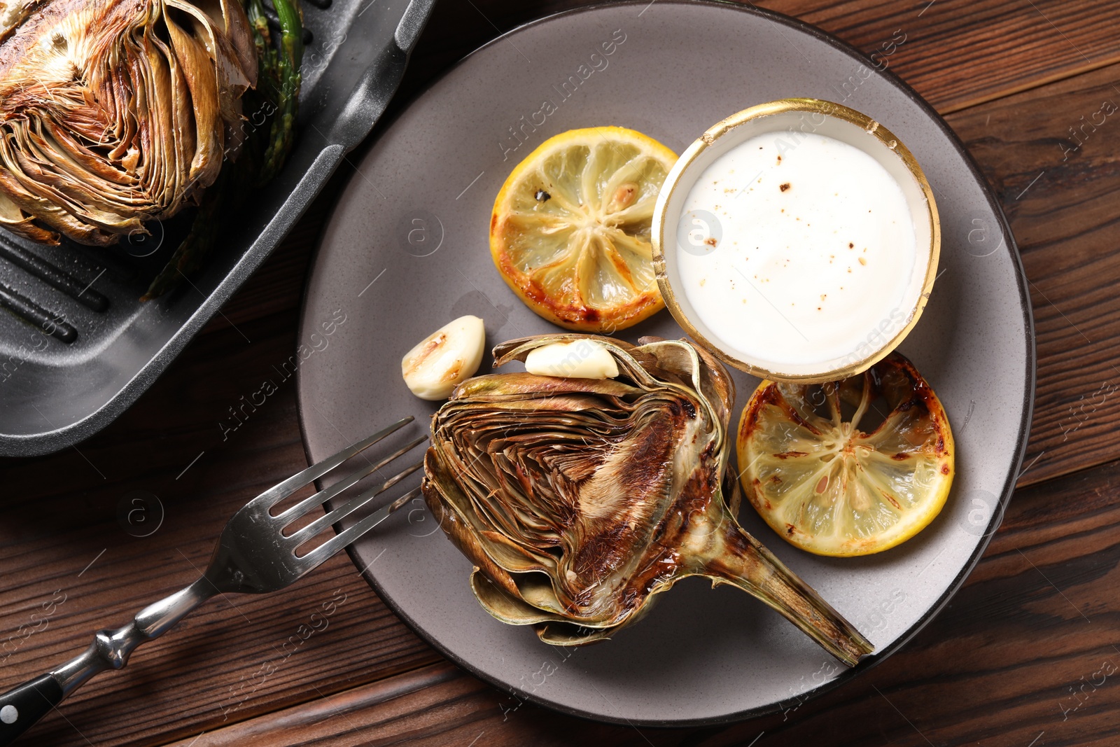 Photo of Tasty grilled artichokes served on wooden table, flat lay