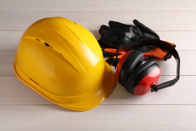 Hard hat, earmuffs and gloves on white wooden table. Safety equipment