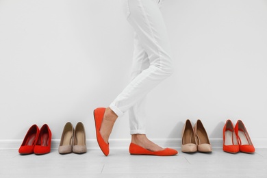 Woman trying on different shoes near white wall, closeup
