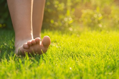 Photo of Teenage girl walking barefoot on green grass outdoors, closeup. Space for text