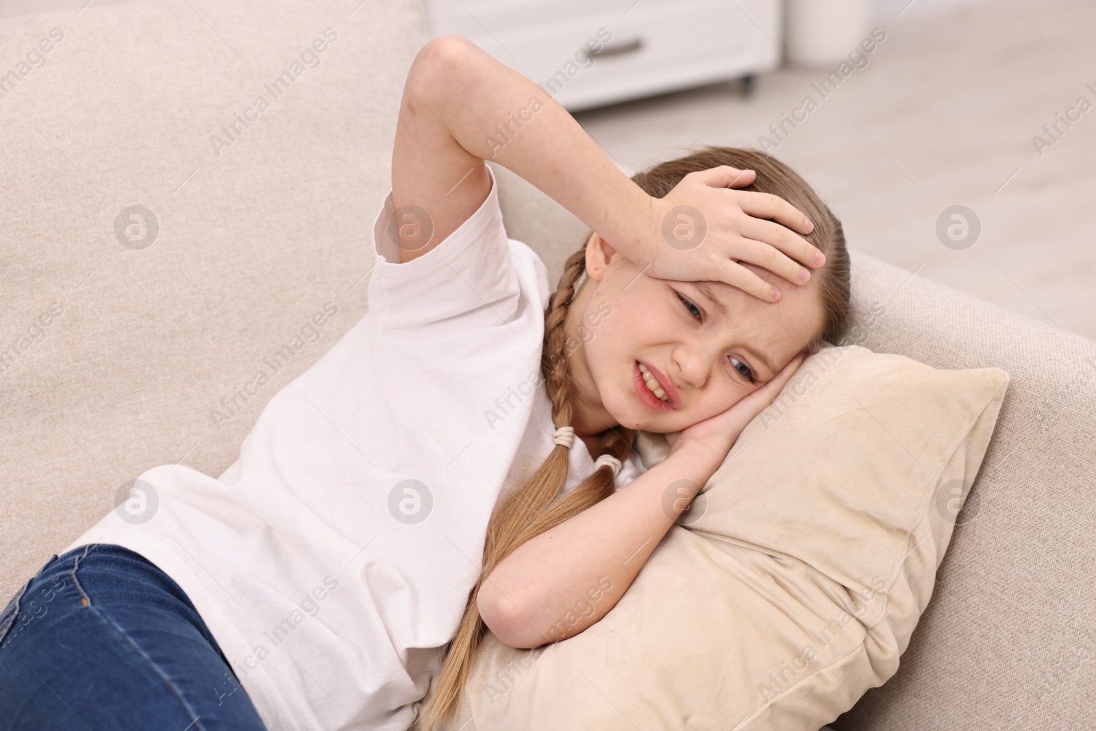 Photo of Little girl suffering from headache on sofa indoors