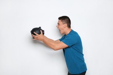 Emotional teenage boy with piggy bank on white background