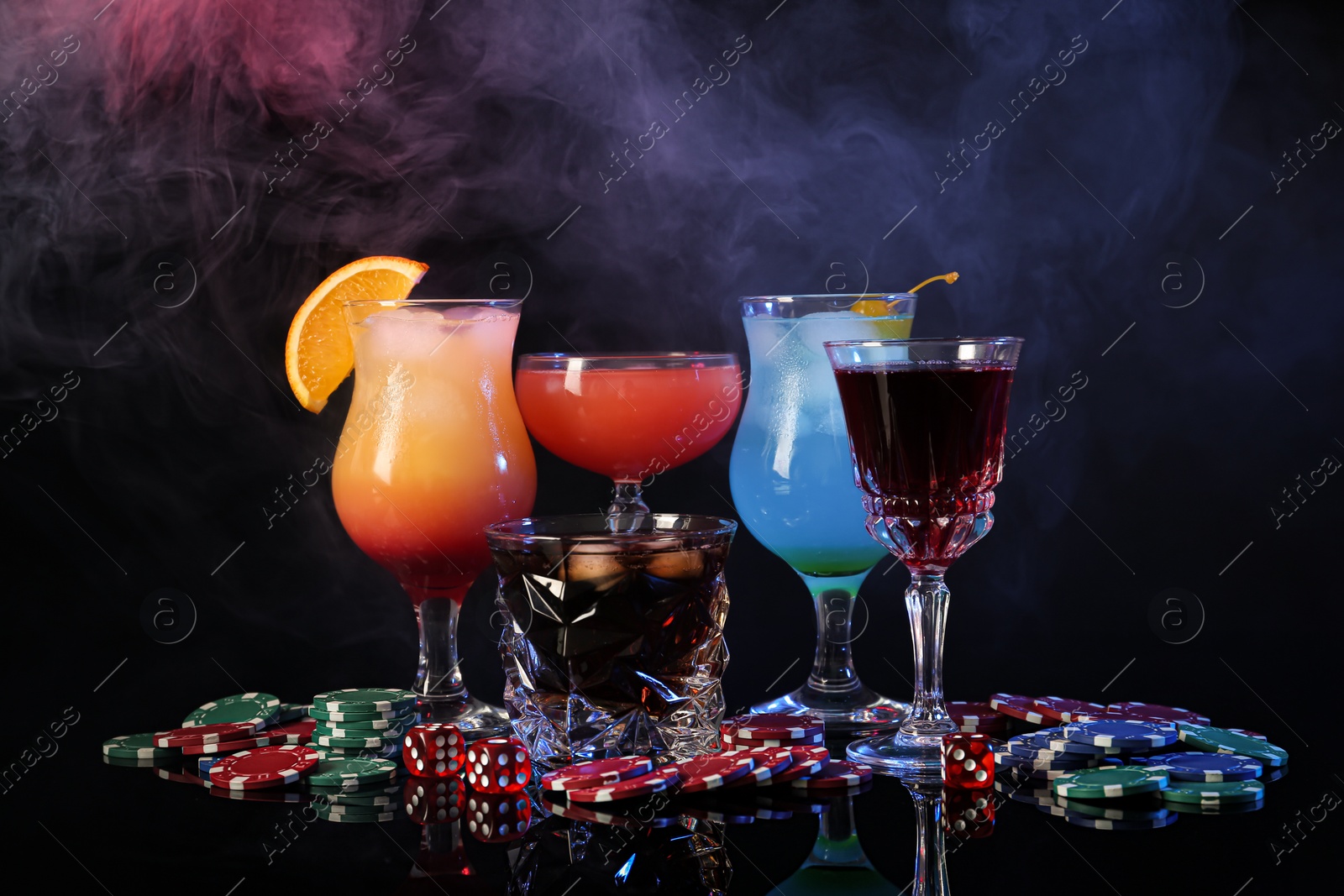 Photo of Casino chips, dice and alcohol drinks on dark background with smoke