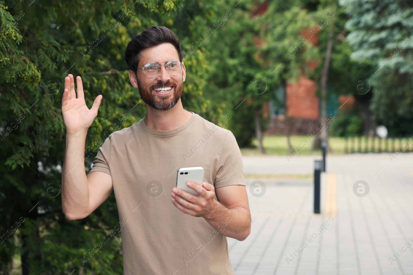 Photo of Smiling handsome bearded man with smartphone outdoors. Space for text