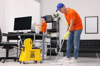 Photo of Cleaning service workers cleaning in office. Bucket with wet floor sign indoors