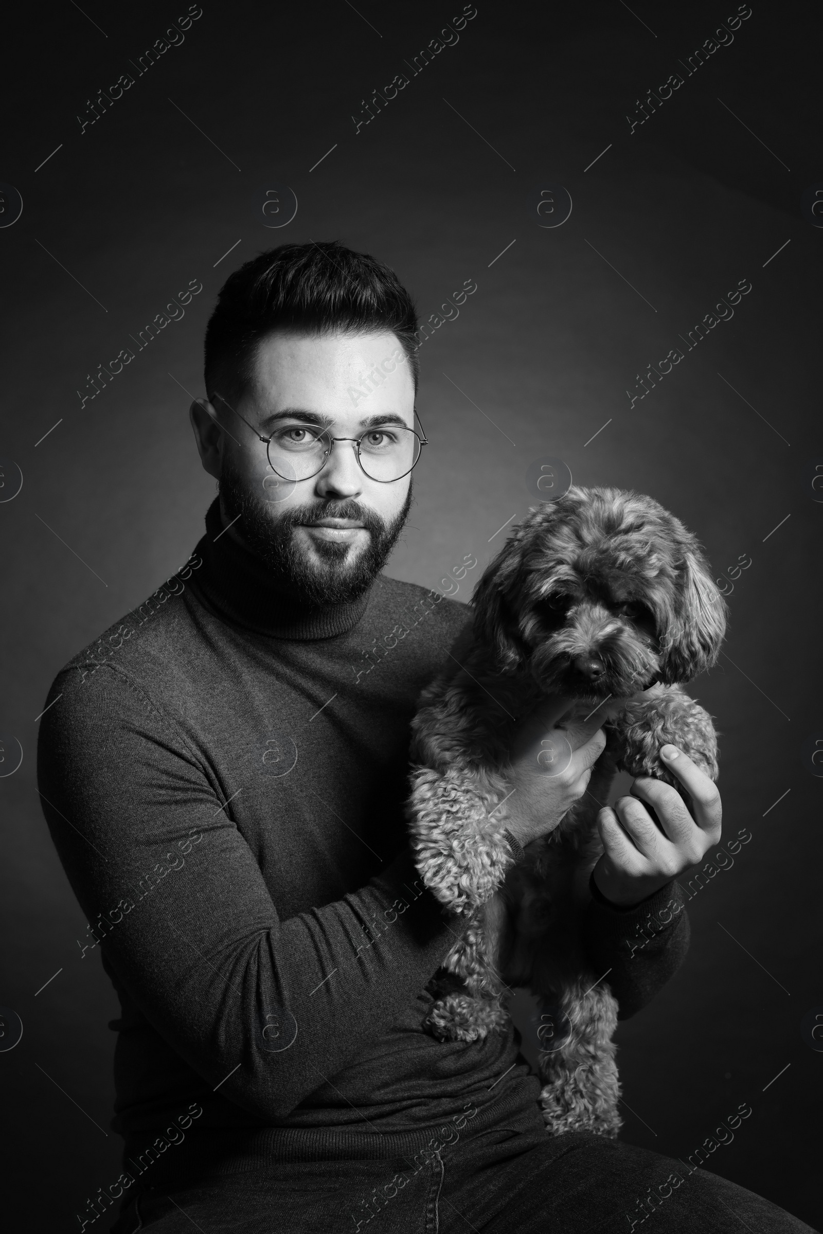 Photo of Handsome bearded man with cute dog on dark background. Black and white effect