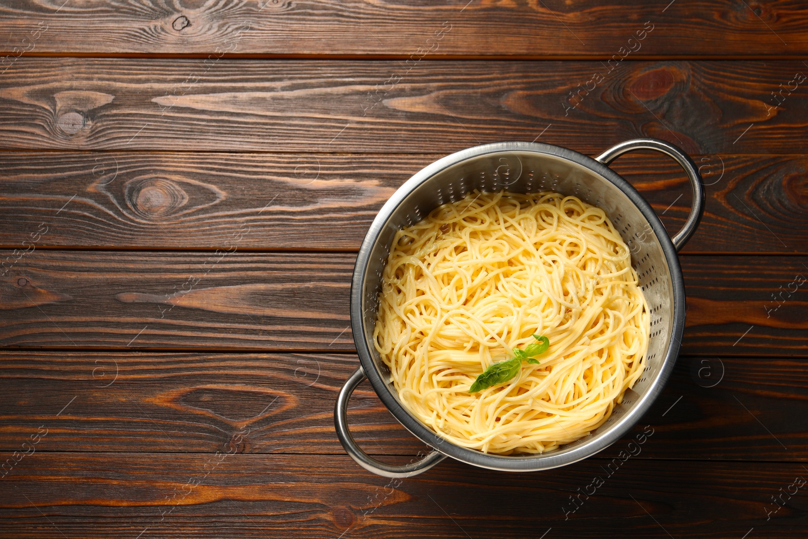 Photo of Cooked pasta in metal colander on wooden table, top view. Space for text
