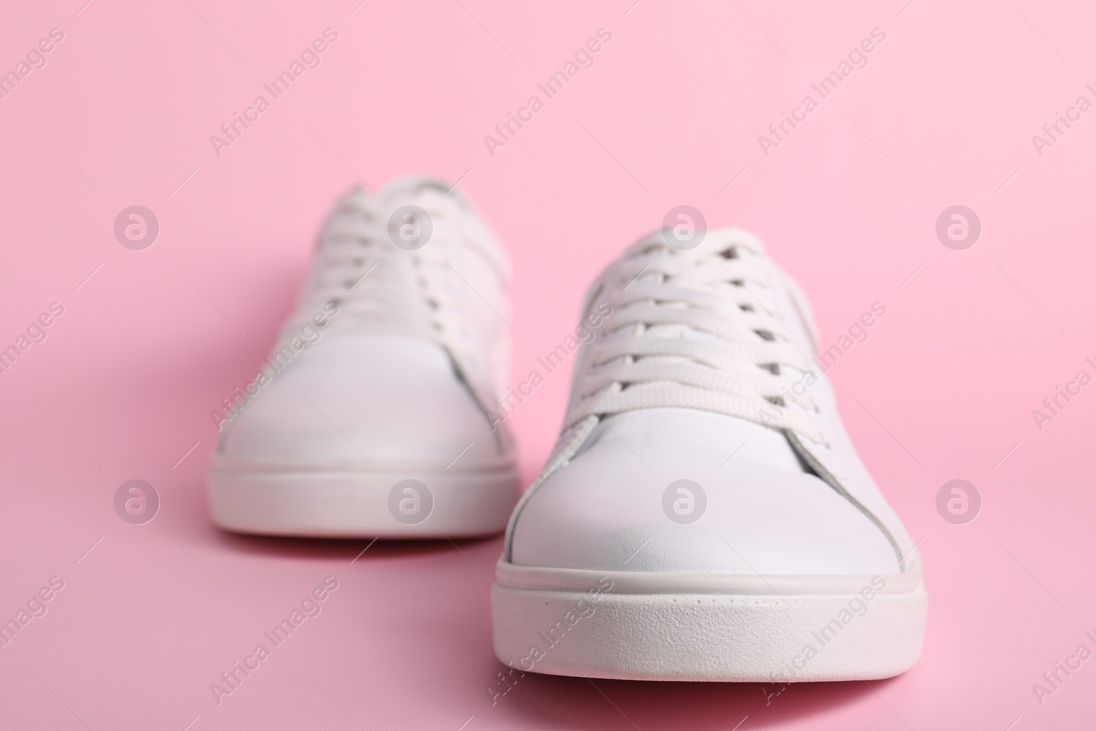 Photo of Pair of stylish white sneakers on pink background, closeup