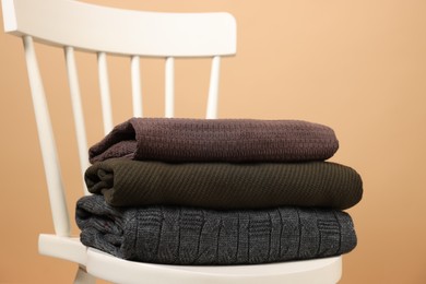 Photo of Stack of different warm sweaters on white chair against beige background, closeup