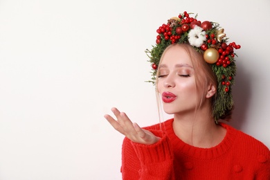 Beautiful young woman wearing Christmas wreath on white background. Space for text