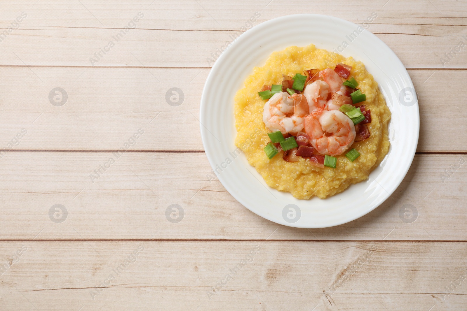 Photo of Plate with fresh tasty shrimps, bacon, grits and green onion on light wooden table, top view. Space for text