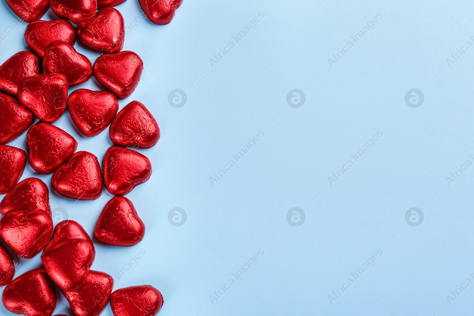 Photo of Heart shaped chocolate candies in red foil on light blue background, flat lay. Space for text